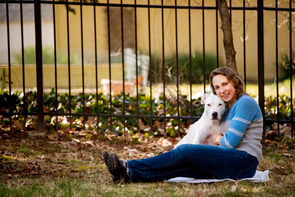Woman sitting with dog in front of fence.