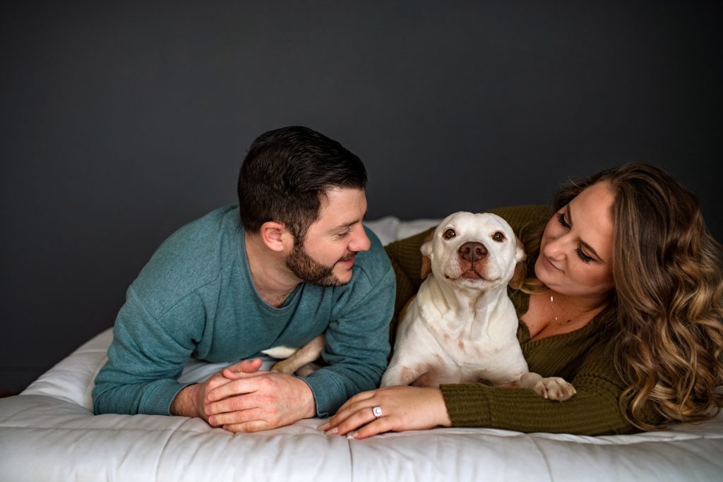 Man and Woman laying on bed with dog.