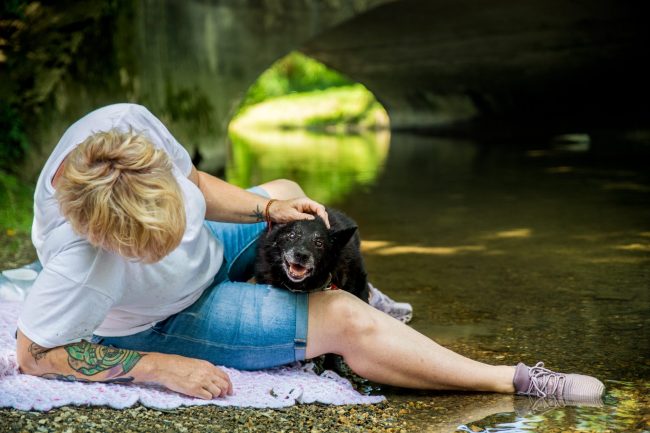 Woman pets and snuggles her dog on a river bank