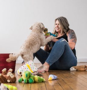 Woman sitting on floor playing with puppy dog.